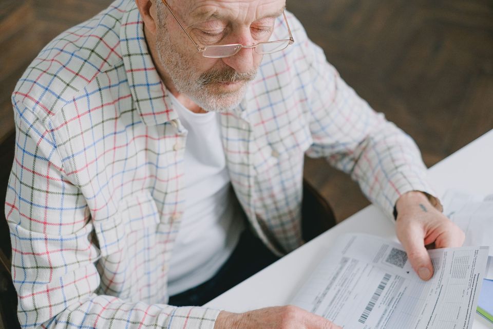 An older man in a checked shirt reading a tax form
