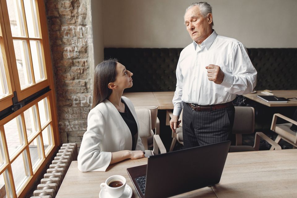 A manager standing and talking with a seated employee at a laptop