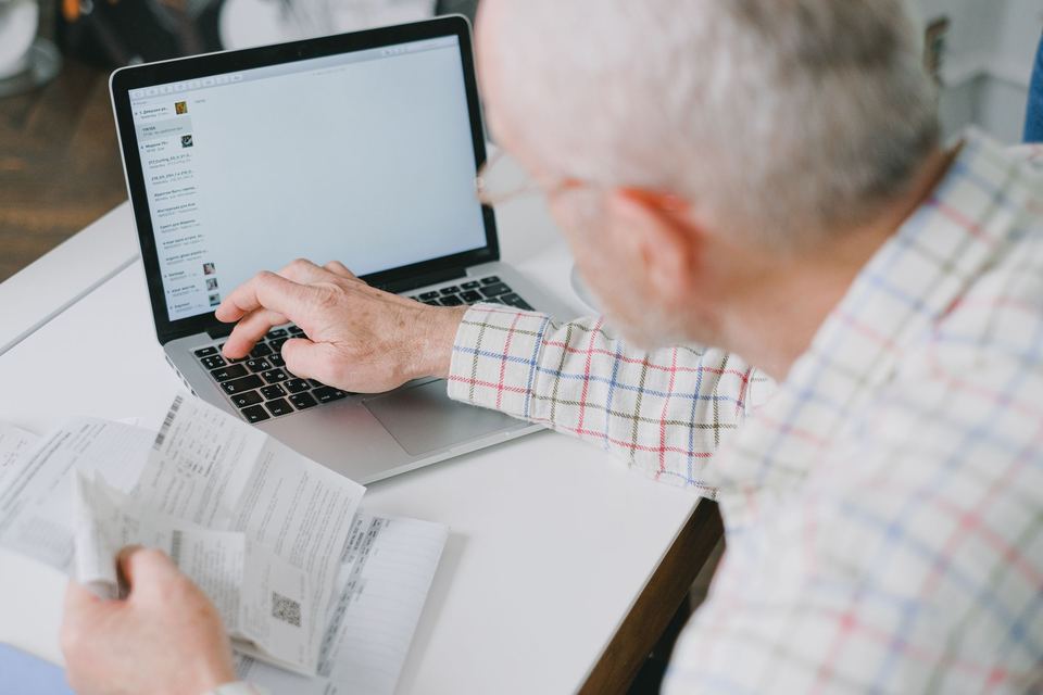 An older man at a laptop with a printed page in his hand