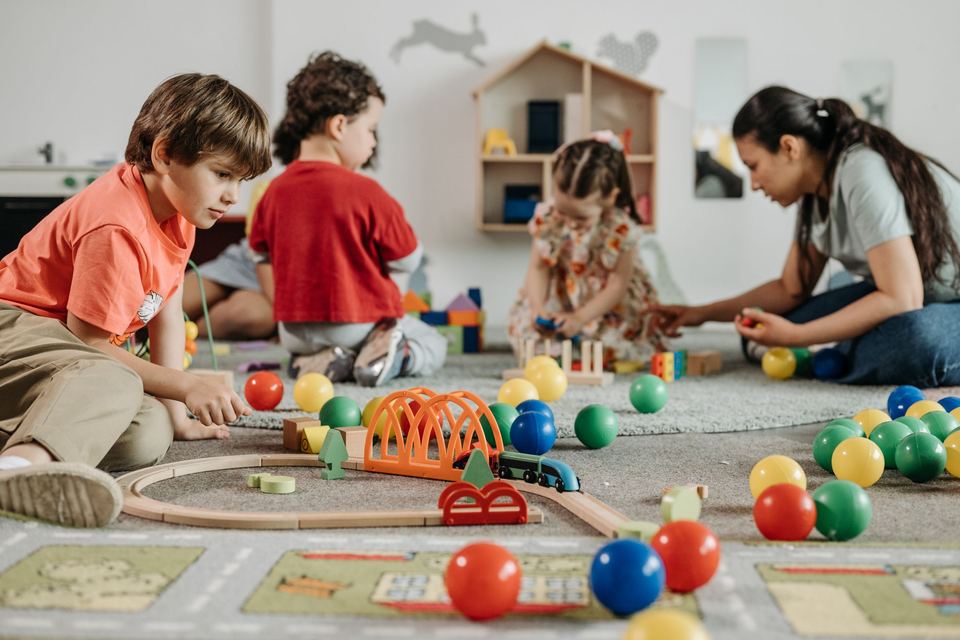 A child care worker sitting on the floor playing with young children