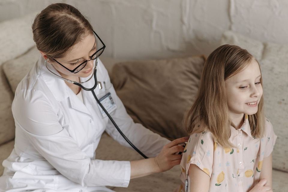 A doctor listening to a young girl's chest with a stethoscope