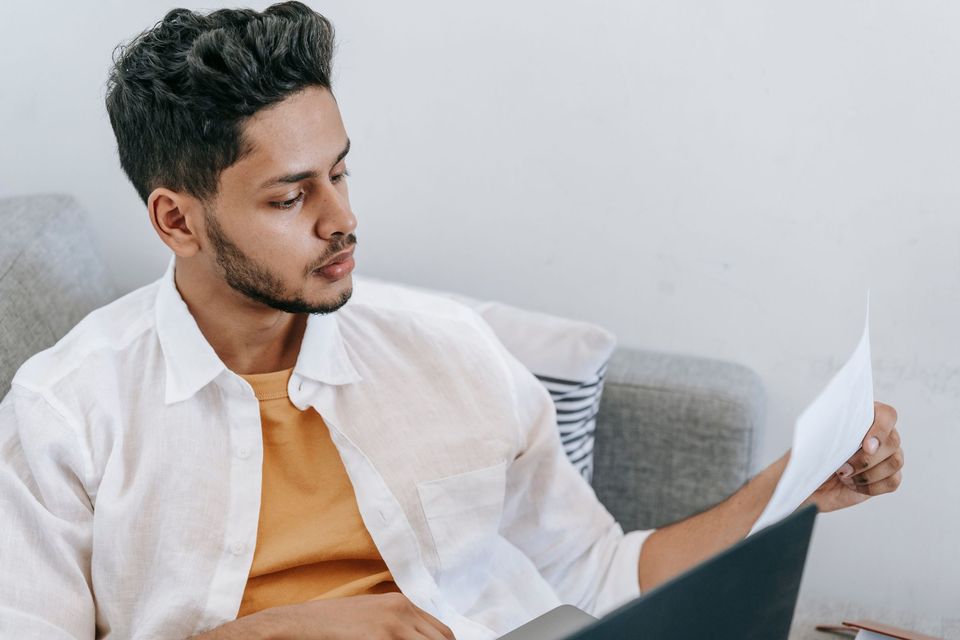 A man sitting on a couch reading a page of paperwork