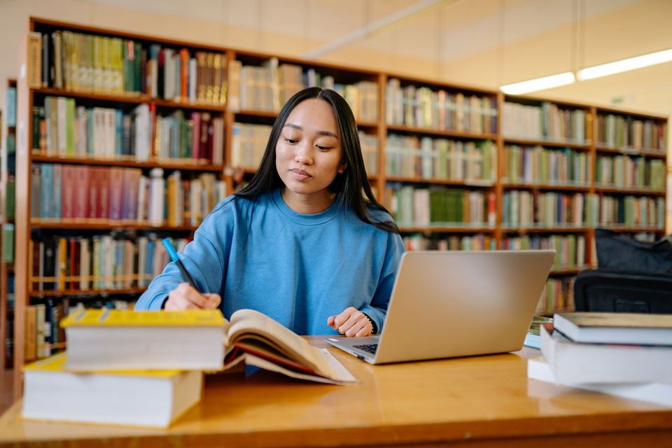 A student studying at a library desk with a laptop and books