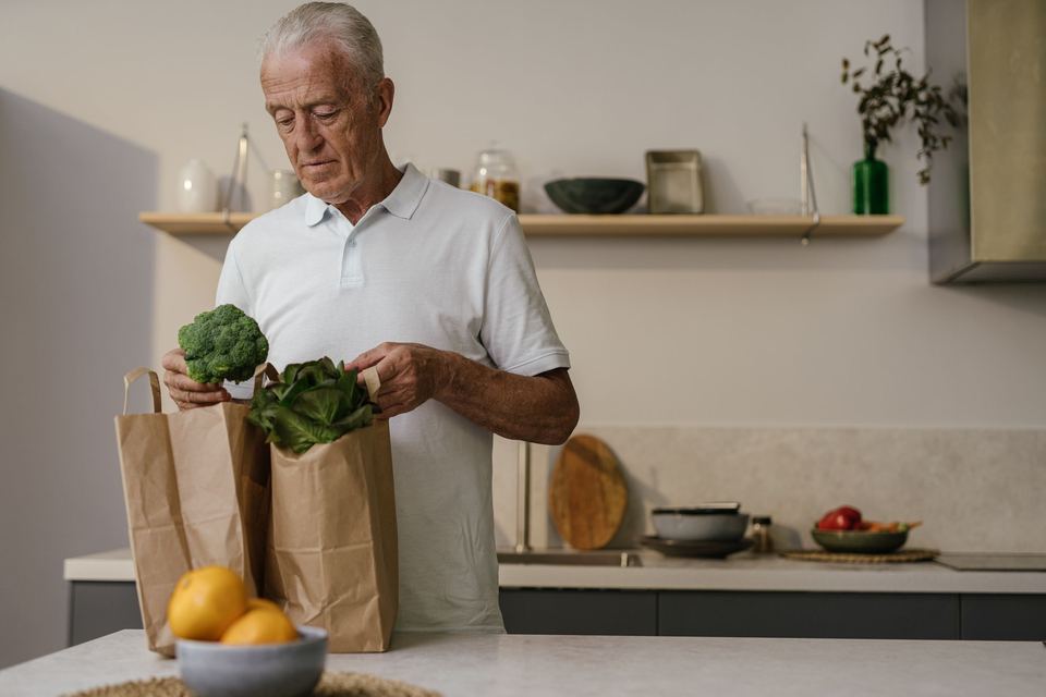 An older man holding a paper bag of groceries in a kitchen