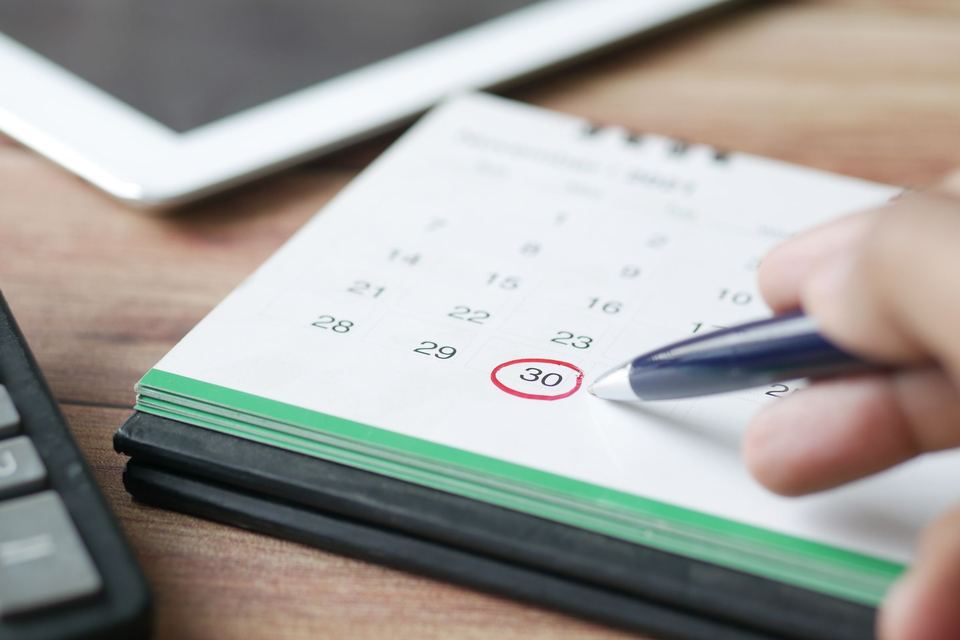 A hand circling the 30th on a desk calendar with a blue pen