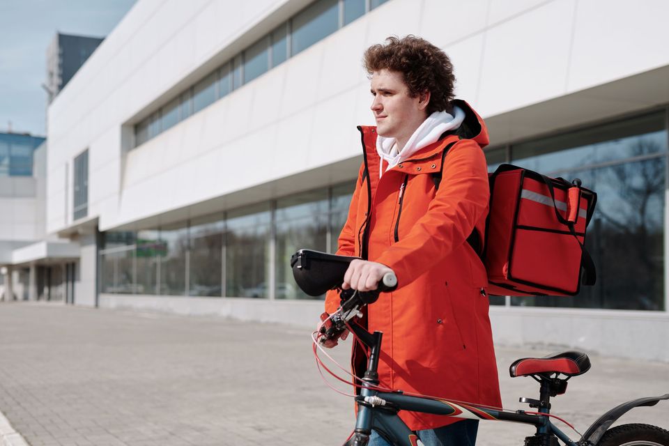 A delivery courier in a red jacket standing with a bicycle and an insulated bag