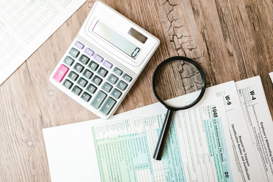 Tax forms on a wooden table with a calculator and a magnifying glass