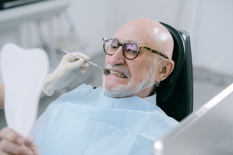 An older man in glasses in a dental chair holding a mirror
