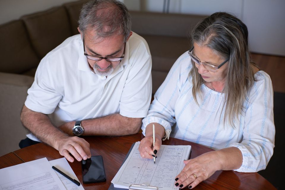 An older man and woman checking figures on a printed form with a pen and a phone