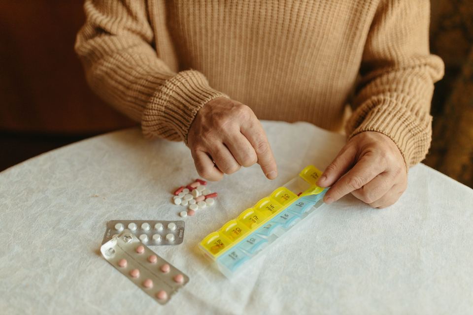 An older person sorting pills into a weekly pill organizer