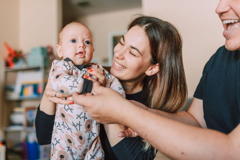 A mother and father holding up a smiling baby at home