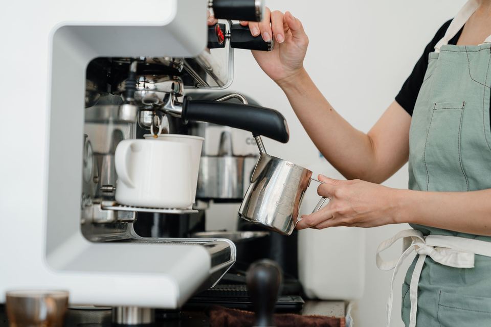 A barista in an apron steaming milk at an espresso machine