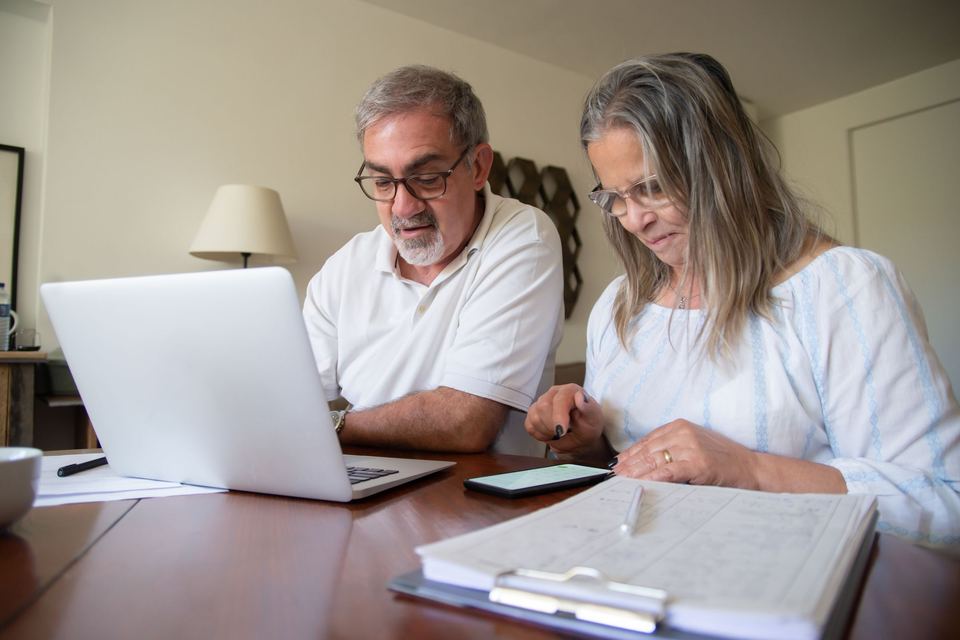 An older couple comparing papers at a table with a laptop