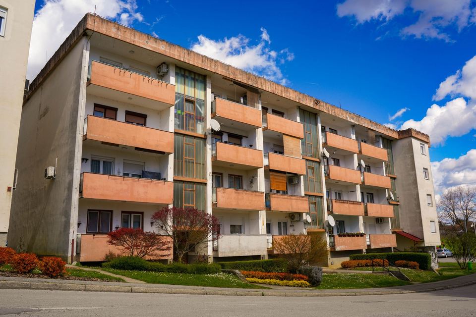 A low-rise brick apartment building with balconies under a blue sky