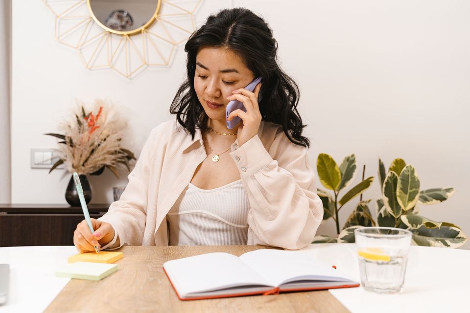 A woman on the phone taking notes in a notebook at her desk