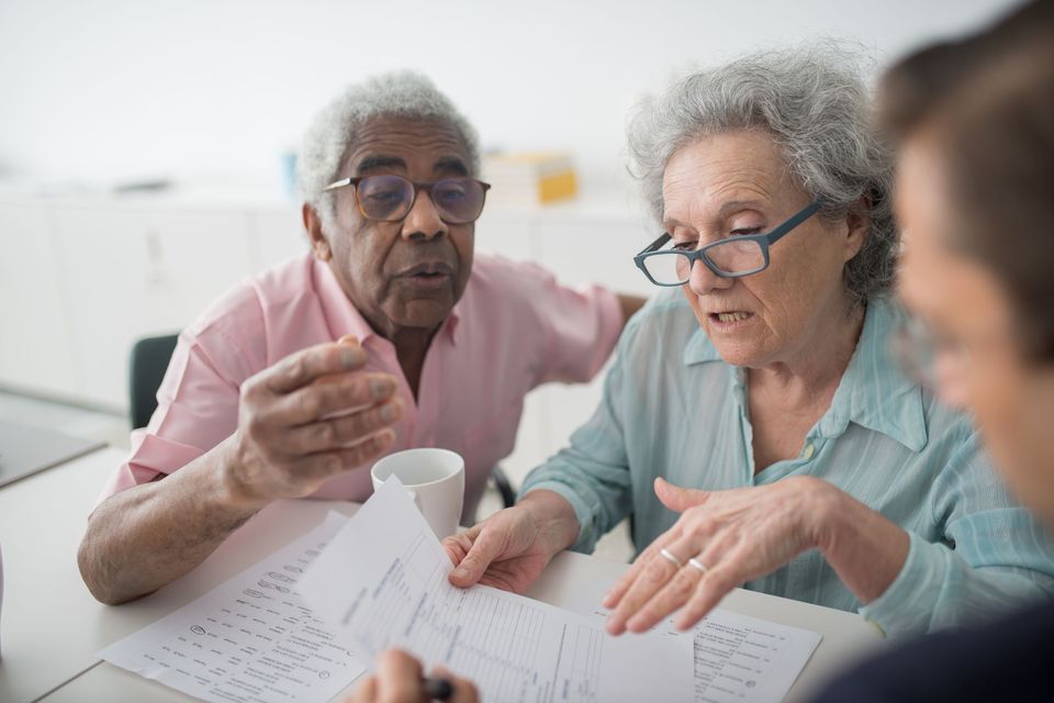 Two older adults going over papers at a table with a younger helper beside them