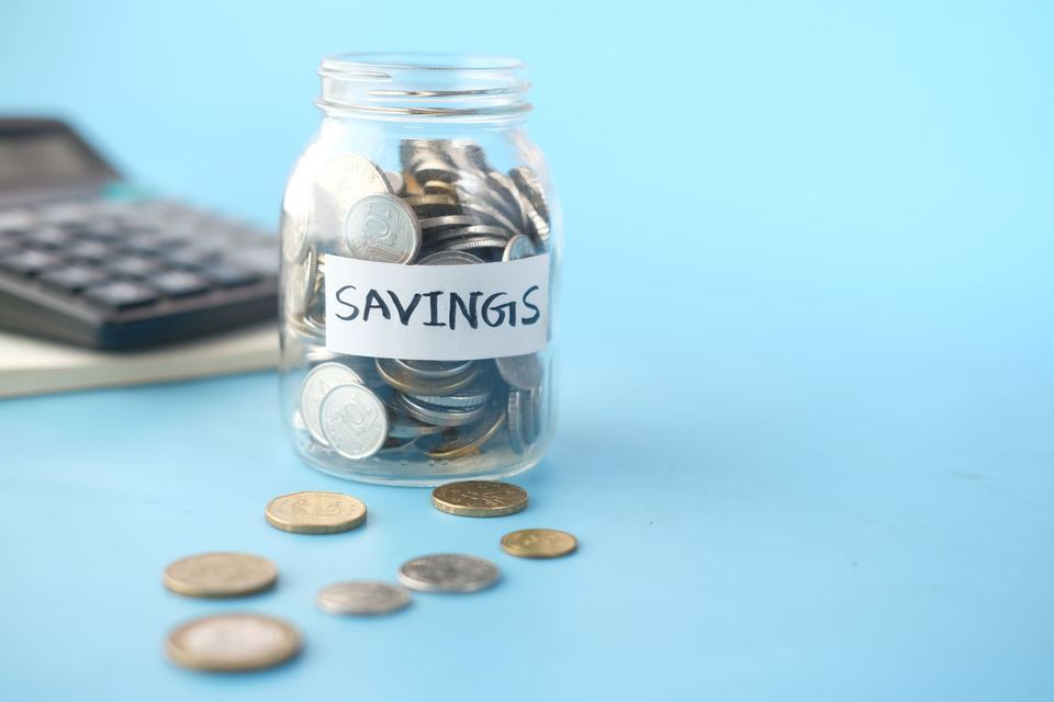 A jar labeled savings with coins and a calculator on a blue table