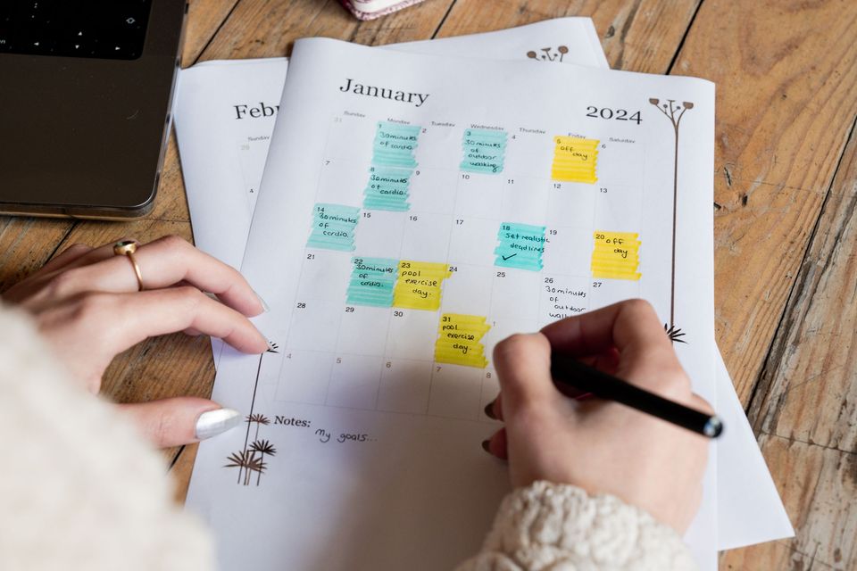 A hand writing on a monthly planner with colored sticky notes