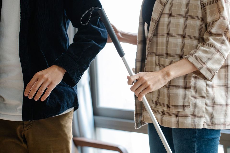 A person with a white cane being guided by a companion