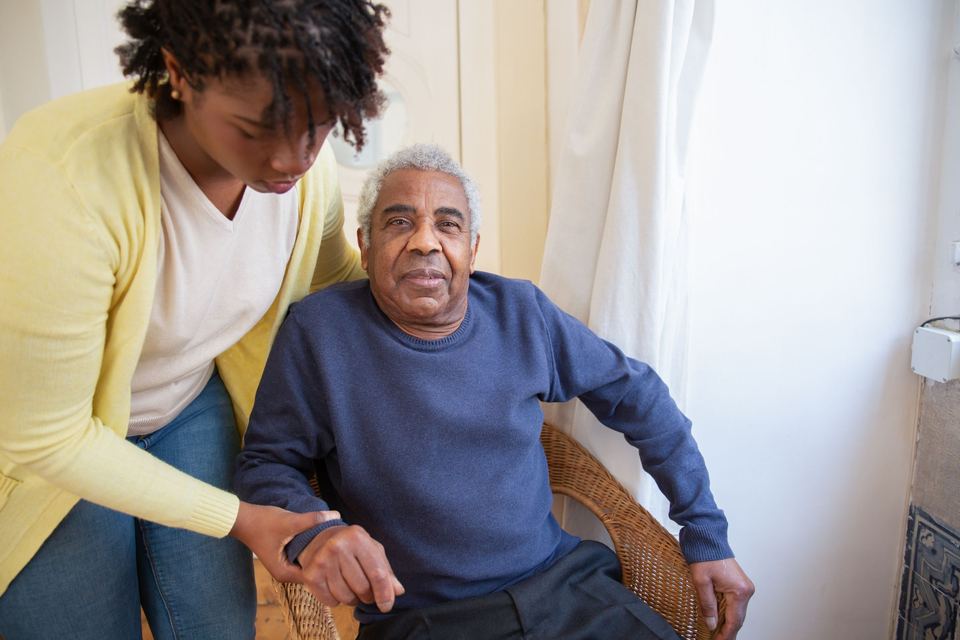 A caregiver sitting beside a smiling older man in a care home room