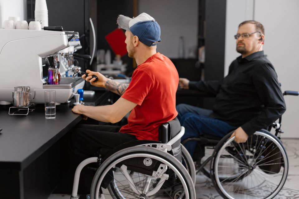 Two men in wheelchairs working together at a coffee counter