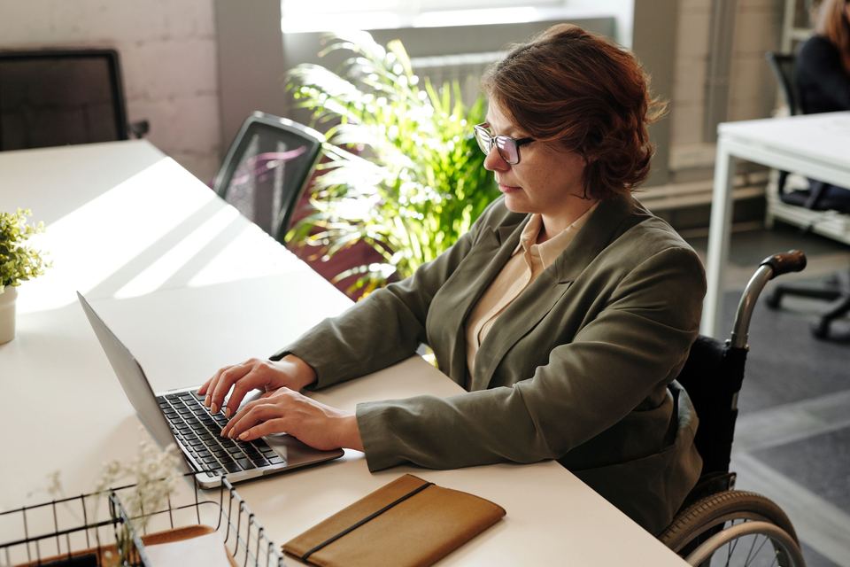 A woman using a wheelchair typing on a laptop at an office desk